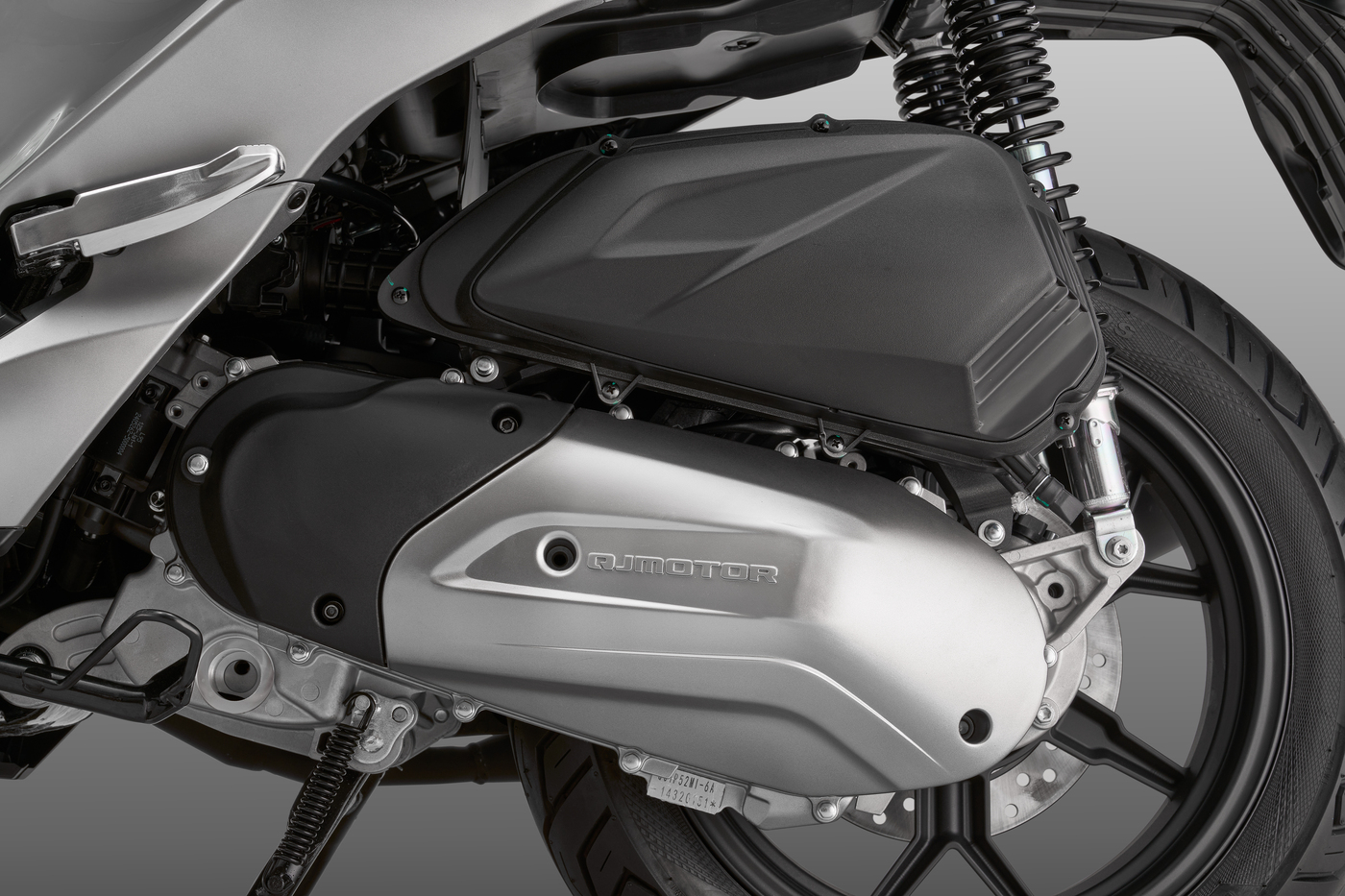 QJMOTOR FORT 125 N: Die seitliche Motor- und Getriebeeinheit neben dem Hinterrad mit silberner Abdeckung.
